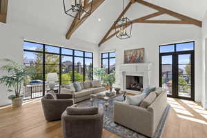 Living room with high vaulted ceiling, light wood finished floors, a fireplace, a chandelier, and beam ceiling