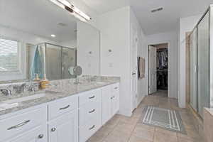 Bathroom featuring a stall shower, light tile patterned flooring, a walk in closet, and double vanity