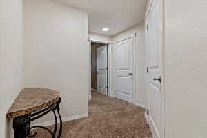Corridor featuring a textured wall and light carpet
