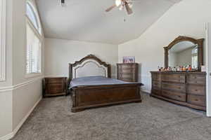 Carpeted bedroom featuring multiple windows, ceiling fan, and vaulted ceiling