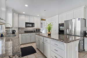 Kitchen with dark stone countertops, black appliances, a center island, white cabinetry, and recessed lighting