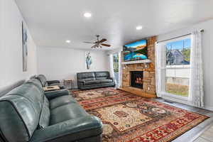Living area featuring wood finished floors, a stone fireplace, ceiling fan, and recessed lighting