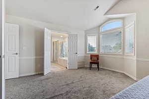 Bedroom featuring vaulted ceiling, light carpet, and ensuite bathroom
