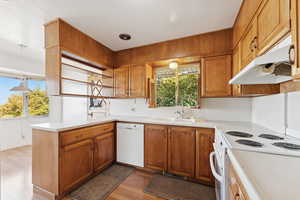 Kitchen featuring a peninsula, brown cabinetry, white appliances, light wood-style floors, and light countertops