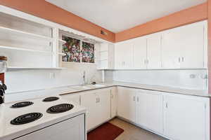 Kitchen with white range with electric cooktop, light countertops, white cabinets, and open shelves