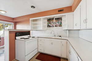 Kitchen with white electric stove, white cabinets, light countertops, and open shelves