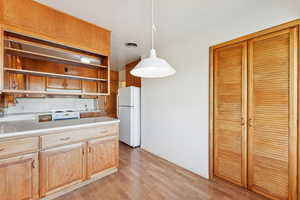 Kitchen featuring light countertops, decorative light fixtures, white appliances, light wood-style floors, and open shelves