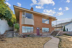 View of front facade featuring stairway, a chimney, brick siding, and a balcony
