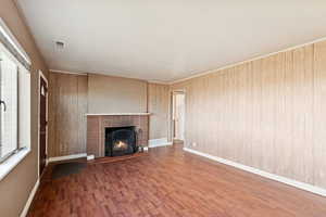 Unfurnished living room with a brick fireplace, wood finished floors, and wooden walls