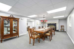 Dining space with light carpet, a paneled ceiling, and a tile fireplace