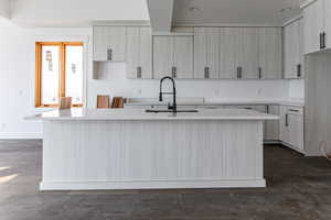 Kitchen with an island with sink, dark wood-style flooring, light stone countertops, and modern cabinets