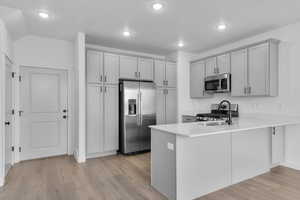 Kitchen featuring appliances with stainless steel finishes, a peninsula, light wood finished floors, recessed lighting, and light stone countertops