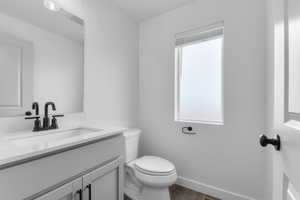 Half bathroom with vanity, healthy amount of natural light, and dark wood-style flooring