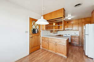 Kitchen featuring white appliances, light countertops, decorative light fixtures, open shelves, and a peninsula