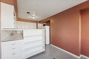 Kitchen with white cabinets, freestanding refrigerator, light countertops, open shelves, and dark aggregate flooring