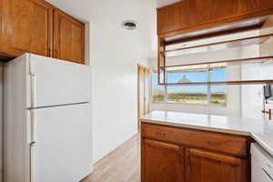 Kitchen featuring brown cabinetry, white appliances, light countertops, and light wood finished floors