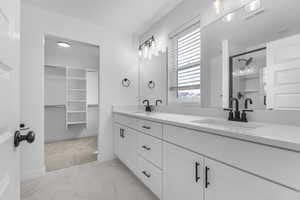 Bathroom featuring double vanity, a walk in closet, a shower stall, and light marble finish floors
