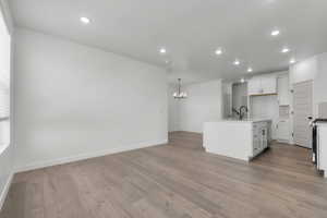 Kitchen featuring white cabinets, recessed lighting, light wood finished floors, decorative backsplash, and a center island with sink