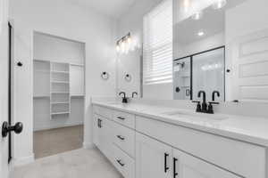Full bathroom featuring a walk in closet, a stall shower, double vanity, and light marble finish flooring