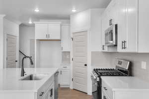 Kitchen featuring stainless steel appliances, light wood-style floors, white cabinetry, light stone counters, and a center island with sink