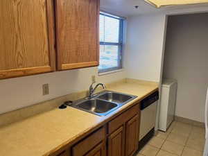 Kitchen with light countertops, light tile patterned flooring, brown cabinets, stainless steel dishwasher, and washer / dryer