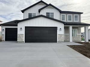 Modern inspired farmhouse with stone siding, driveway, roof with shingles, board and batten siding, and covered porch