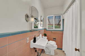 Bathroom with light tile patterned floors, tile walls, a wainscoted wall, and a shower with curtain