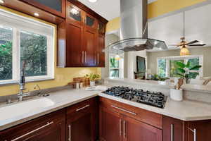 Kitchen featuring island exhaust hood, light stone countertops, a peninsula, black gas cooktop, and open floor plan