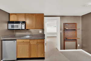 Kitchen featuring stainless steel fridge, white microwave, light colored carpet, and dark countertops
