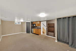 Kitchen with dark countertops, light colored carpet, brown cabinetry, stainless steel dishwasher, and open floor plan