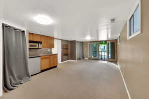 Kitchen featuring light carpet, white microwave, dishwasher, open floor plan, and brown cabinets