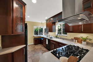 Kitchen featuring hanging light fixtures, recessed lighting, glass insert cabinets, stone finish flooring, and island range hood