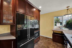 Kitchen with glass insert cabinets, black appliances, stone finish flooring, recessed lighting, and dark brown cabinets