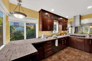 Kitchen featuring a peninsula, pendant lighting, stone finish floors, dishwasher, and island exhaust hood