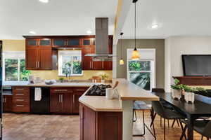 Kitchen with pendant lighting, a peninsula, black appliances, island range hood, and a breakfast bar area