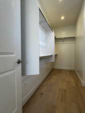 Spacious primary bedroom walk-in closet with light engineered hardwood floors