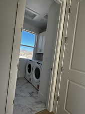 Laundry room with light marble finish floors, washer and clothes dryer, a textured ceiling, and cabinet space