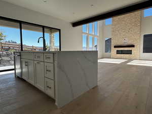 Kitchen with white cabinetry, light engineered hardwood flooring, a fireplace, light stone countertops, and open floor plan