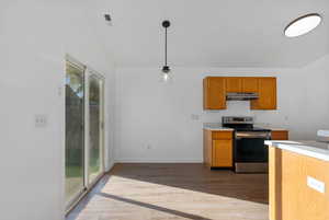 Kitchen featuring light countertops, dark wood finished floors, stainless steel range with electric cooktop, pendant lighting, and brown cabinets