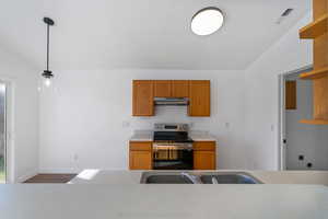 Kitchen with light countertops, stainless steel electric range, open shelves, hanging light fixtures, and brown cabinetry
