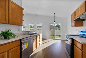 Kitchen with stainless steel appliances, brown cabinetry, light countertops, vaulted ceiling, and light wood-style floors