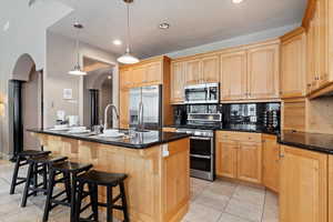 Kitchen with appliances with stainless steel finishes, a kitchen bar, arched walkways, dark stone counters, and a center island with sink