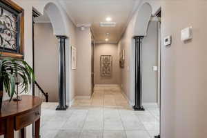 Hallway featuring light tile patterned flooring, ornate columns, ornamental molding, recessed lighting, and arched walkways