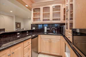 Kitchen featuring dark stone counters, tasteful backsplash, glass insert cabinets, light brown cabinets, and recessed lighting