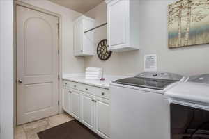 Washroom with light tile patterned floors, washing machine and clothes dryer, and cabinet space