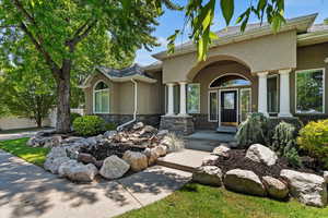 Doorway to property featuring stucco siding, stone siding, and covered porch