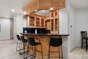 Kitchen featuring light tile patterned floors, a breakfast bar, backsplash, glass insert cabinets, and recessed lighting