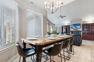 Dining area with vaulted ceiling, a chandelier, a fireplace, light tile patterned flooring, and ceiling fan