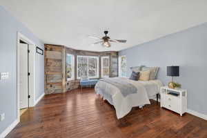 Bedroom with dark wood-style flooring, ceiling fan, wood walls, an accent wall, and a textured ceiling