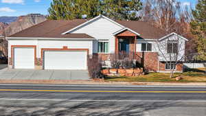 Ranch-style home featuring stone siding, an attached garage, a mountain view, concrete driveway, and roof with shingles